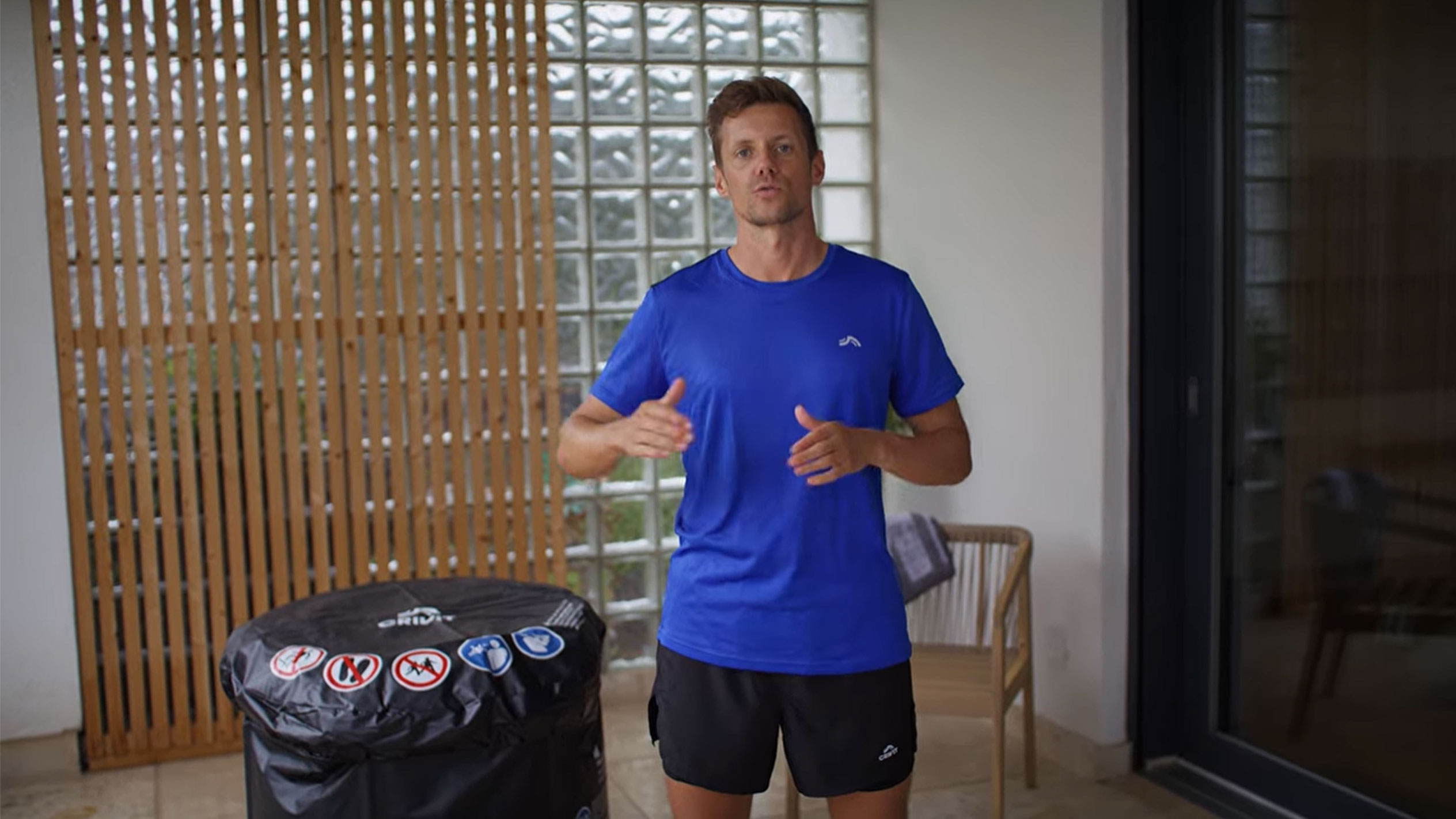 Άνδρας με μπλε μπλουζάκι και μαύρο σορτς, δίπλα σε μαύρο κάλυμμα υδρομασάζ.