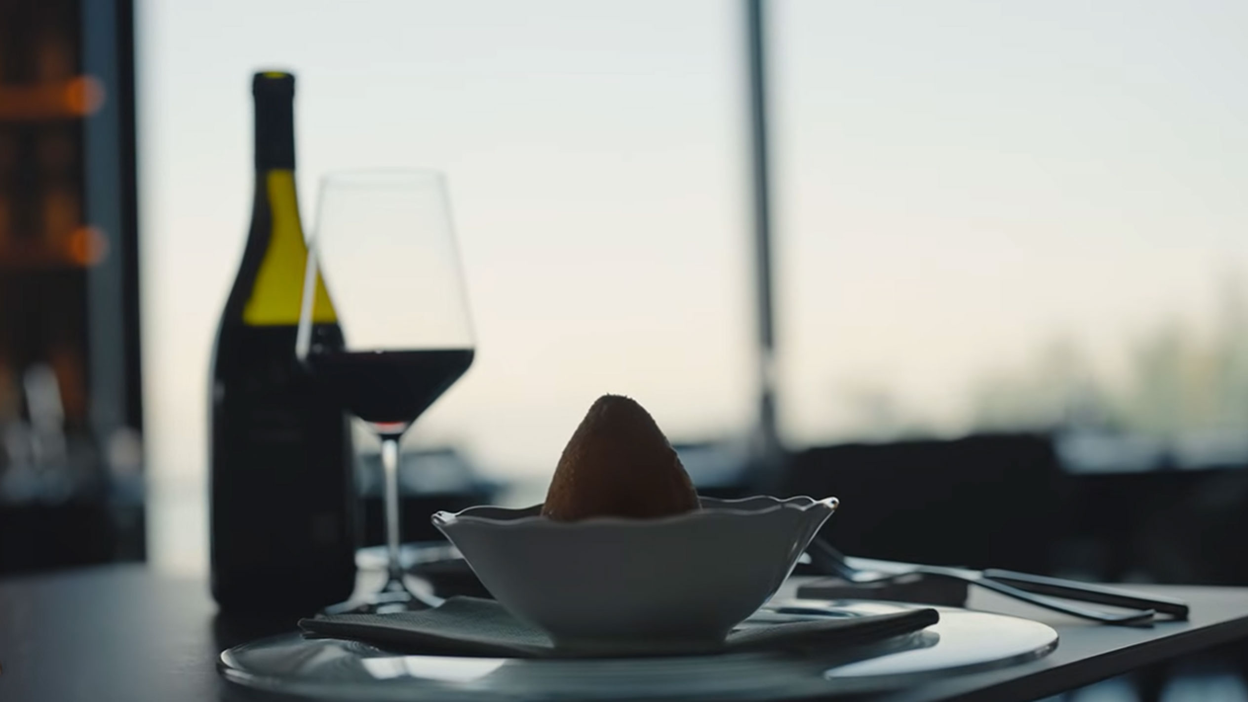 Ένα μπουκάλι κόκκινο κρασί και ένα ποτήρι δίπλα σε ένα αραντσίνο σε ένα μπολ σε ένα τραπέζι.