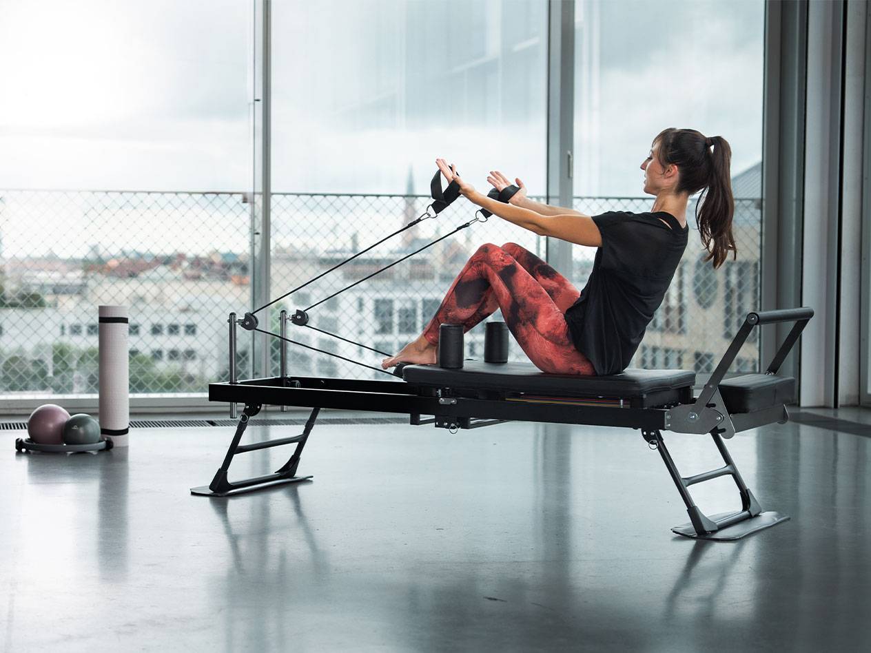 Γυναίκα κάνει Pilates σε reformer με θέα στην πόλη.