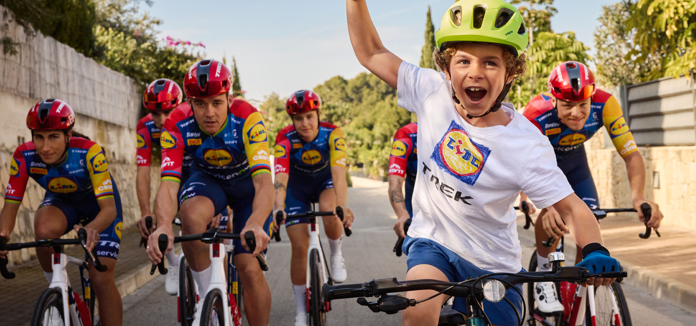 Παιδί με κράνος και μπλουζάκι με το λογότυπο Lidl, περιτριγυρισμένο από ποδηλάτες.