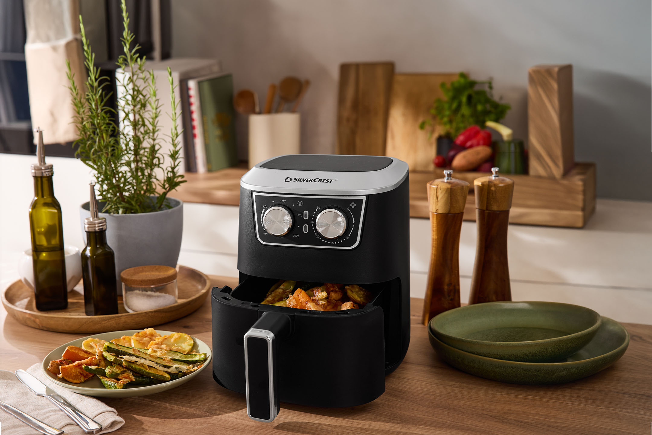 Φριτέζα αέρος με ψητά λαχανικά, ελαιόλαδο, αλάτι και πιπέρι σε πάγκο κουζίνας.