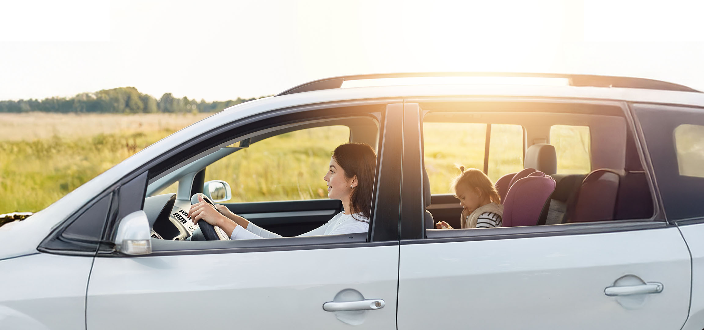 Uma mulher dirige um carro com sua filha no banco de trás.