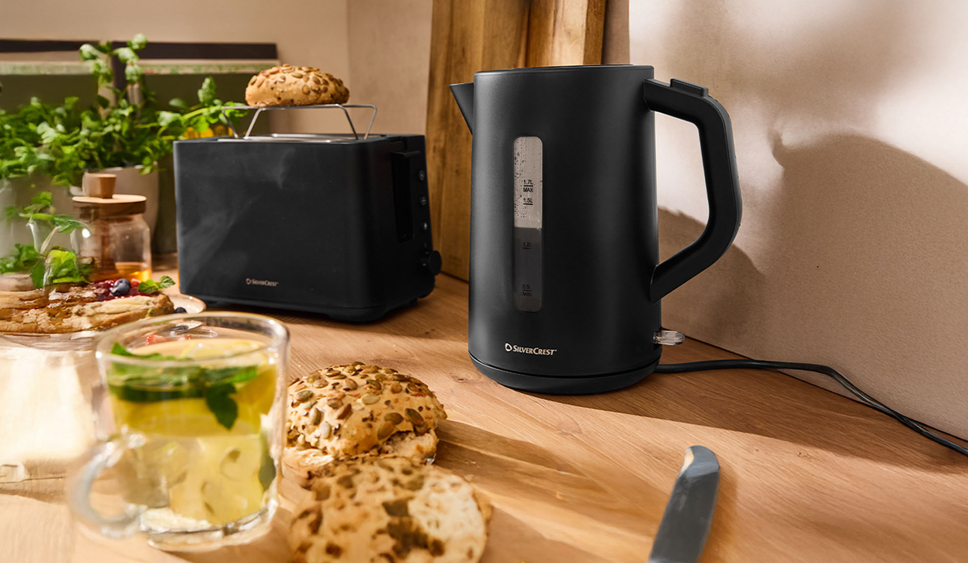 Μαύρος βραστήρας και τοστιέρα SilverCrest σε ξύλινο τραπέζι με πρωινό.