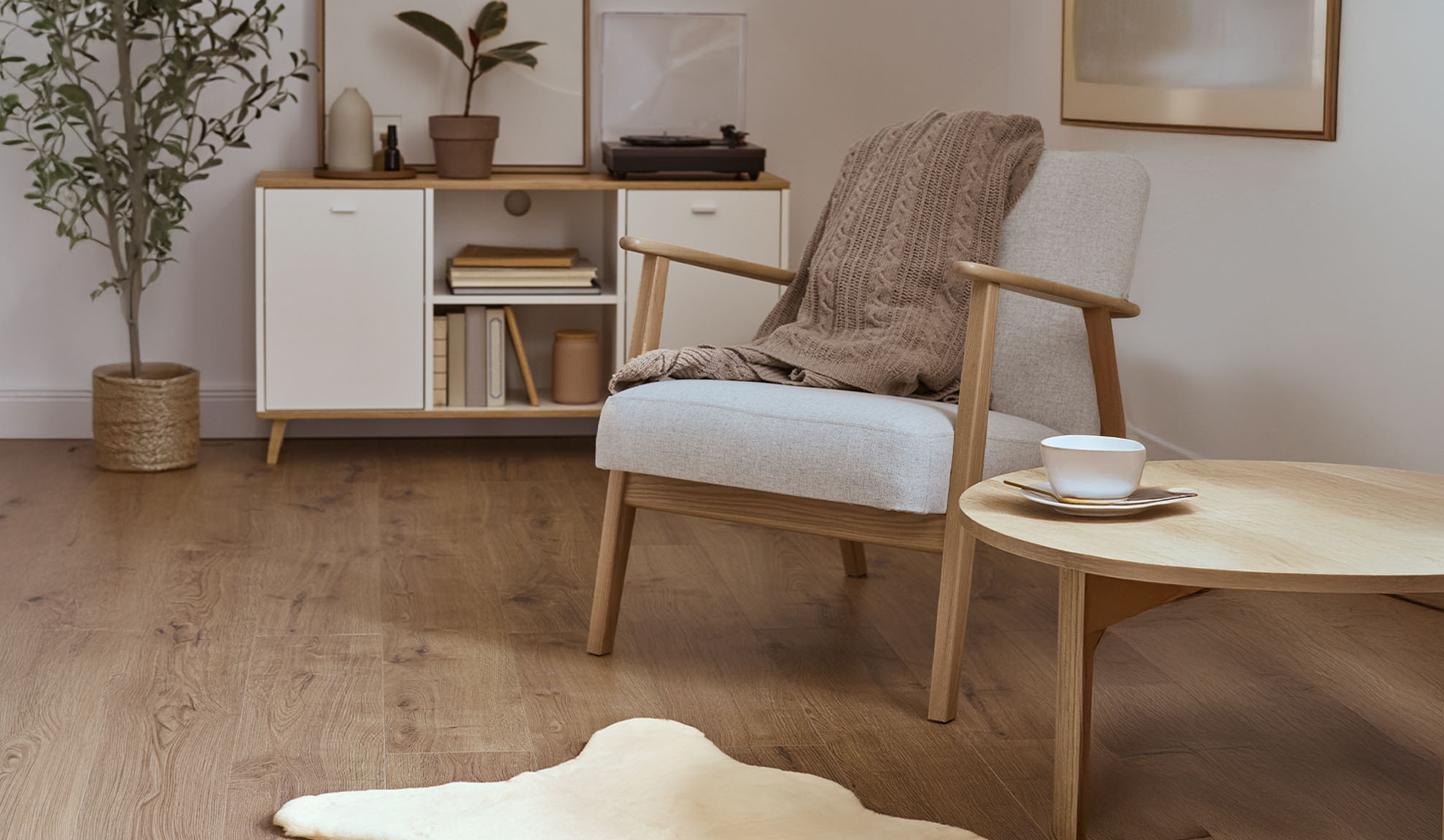 Άνετη πολυθρόνα με κουβέρτα, ξύλινο τραπεζάκι σαλονιού και ντουλάπι αποθήκευσης σε φωτεινό σαλόνι.