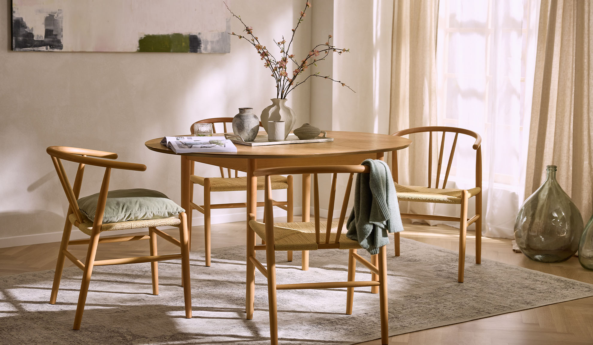 Φωτεινή τραπεζαρία με στρογγυλό ξύλινο τραπέζι, ξύλινες καρέκλες με ψάθινα καθίσματα και λουλουδάτη διακόσμηση.