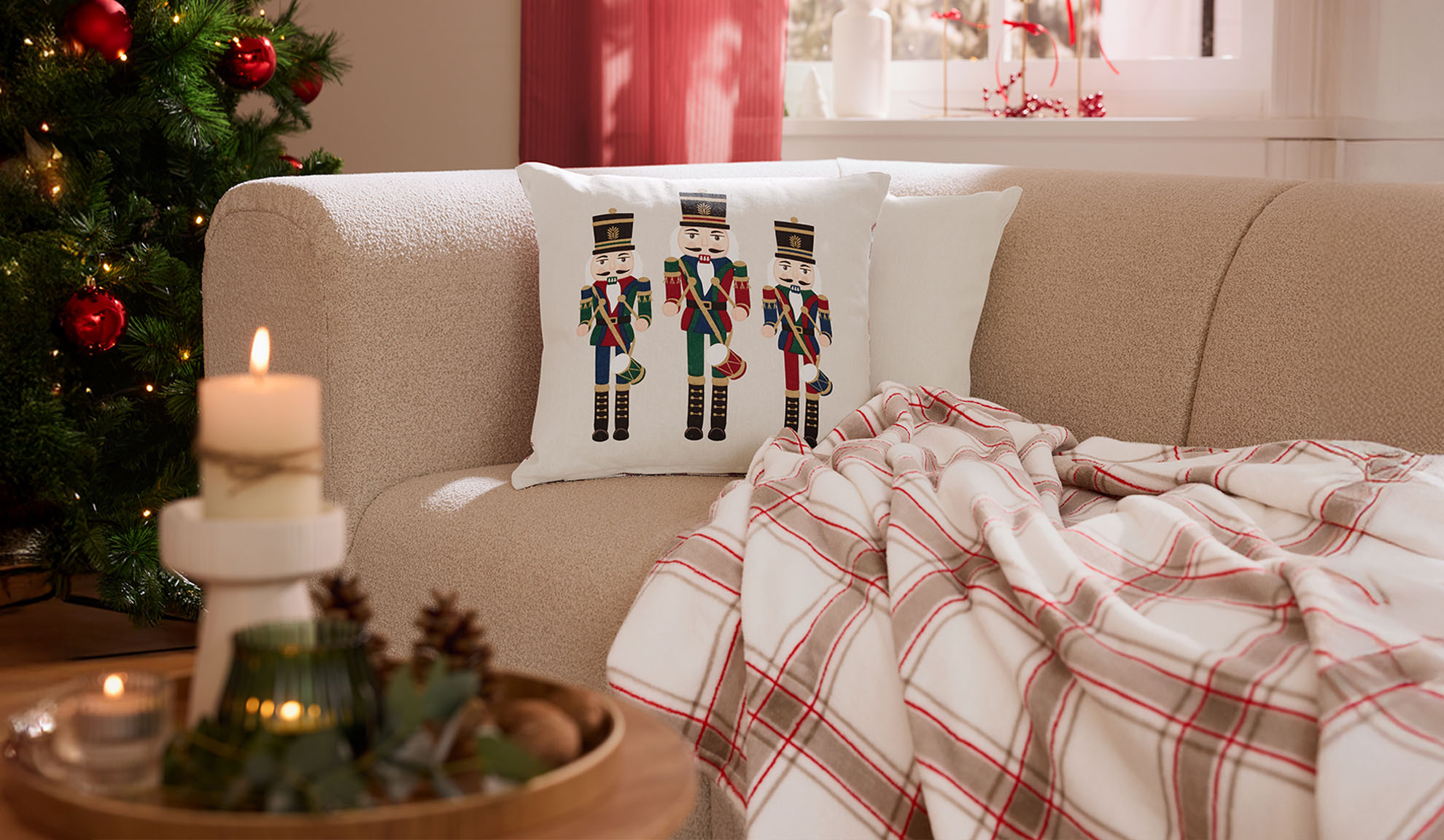 Χριστουγεννιάτικο σαλόνι με καναπέ, μαξιλάρια καρυοθραύστη, καρό ριχτάρι και κεριά.