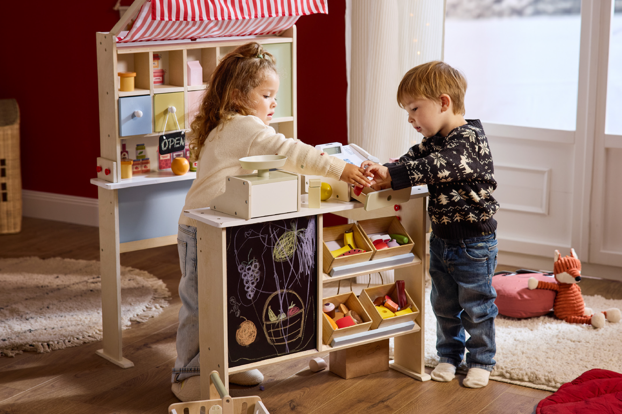 Δύο παιδιά παίζουν με ένα ξύλινο παιχνίδι μανάβικο με ταμειακή μηχανή και ζυγαριά.