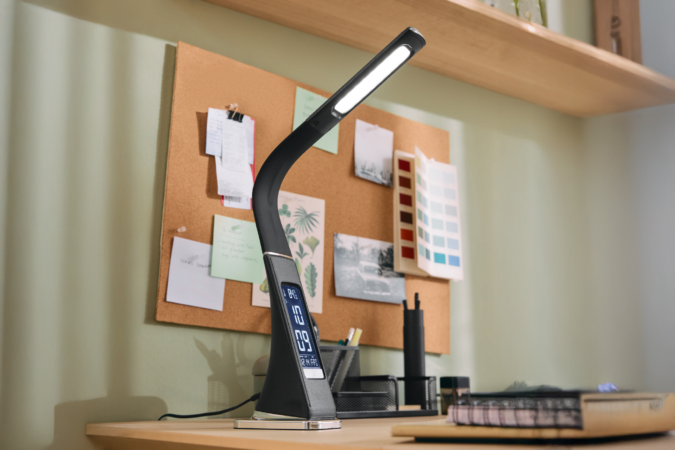 Λάμπα γραφείου με οθόνη, πίνακας φελλού και ράφι σε γραφείο.