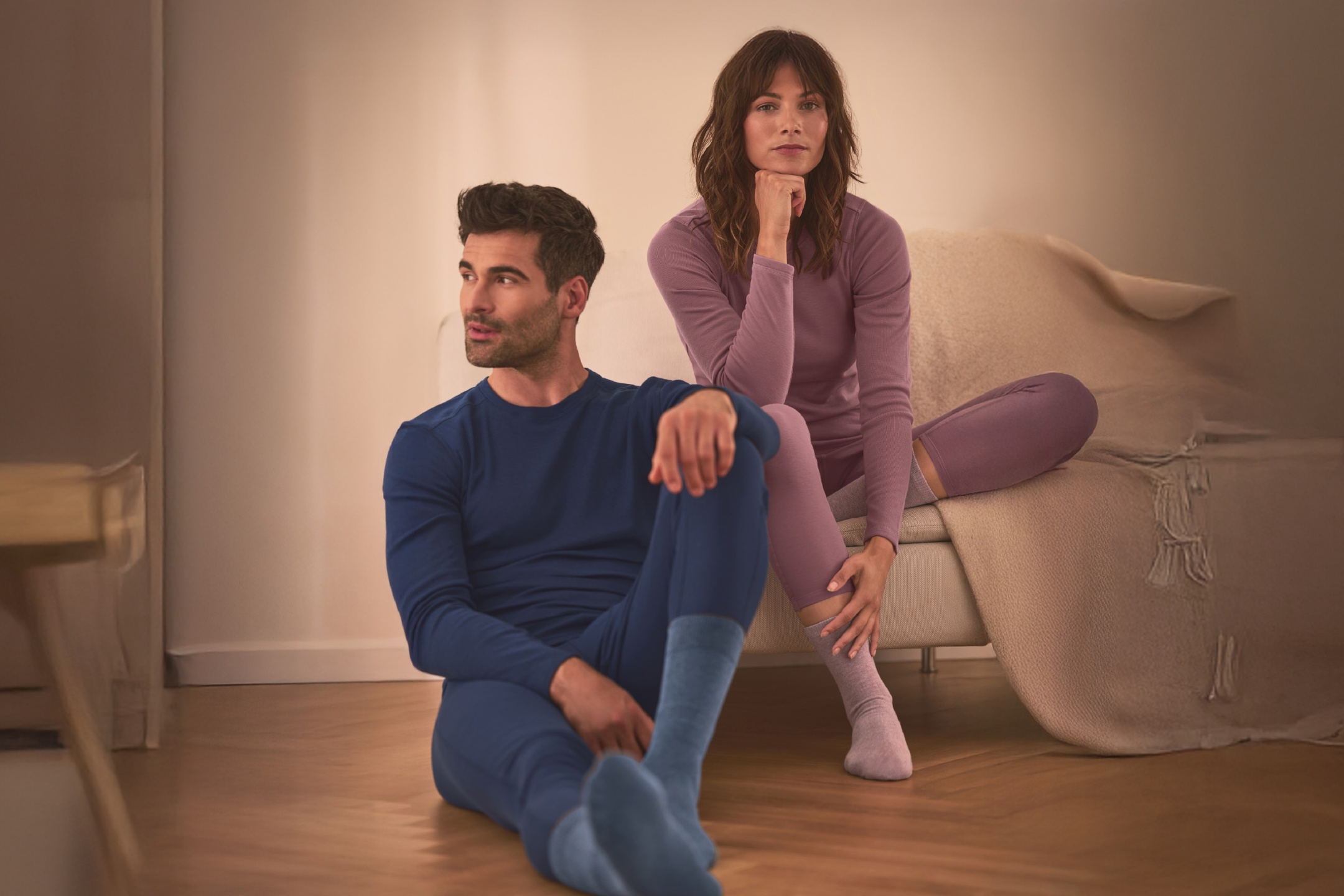 Άνδρας και γυναίκα φορούν άνετα εσώρουχα, ο άνδρας κάθεται στο πάτωμα, η γυναίκα στον καναπέ.