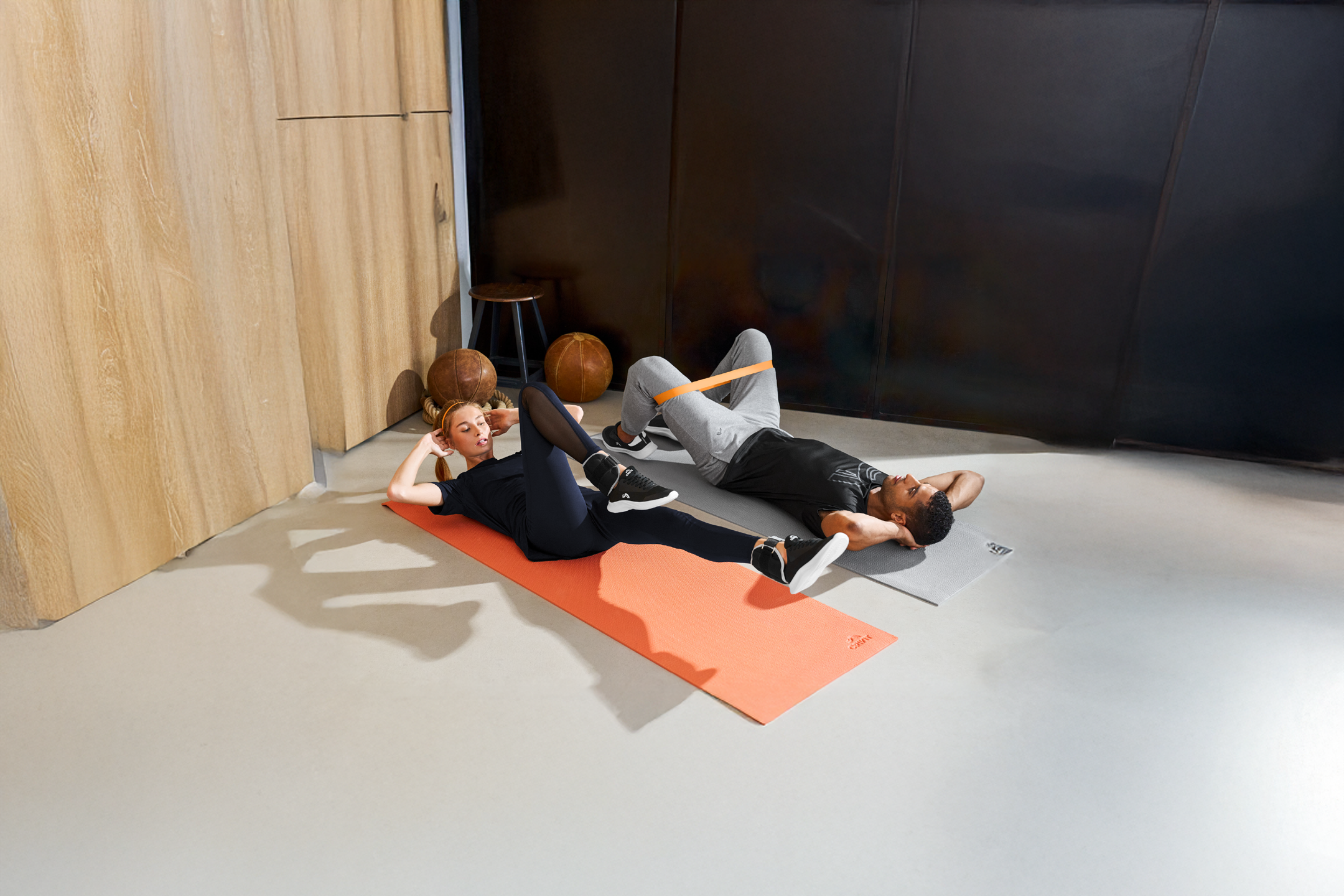 Δύο άτομα κάνουν κοιλιακούς σε στρώματα γιόγκα, με τον άνδρα να χρησιμοποιεί έναν ιμάντα αντίστασης.