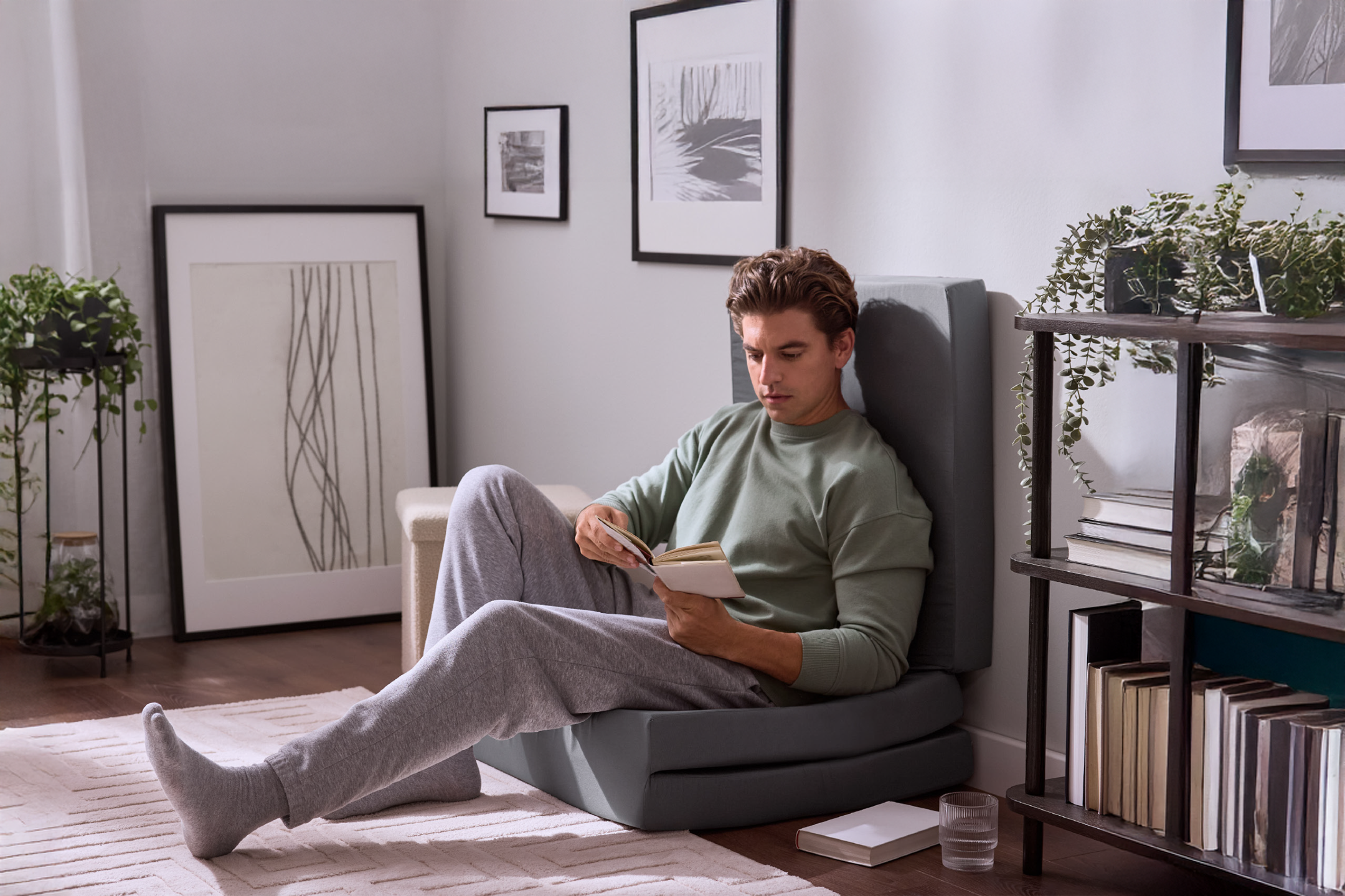 Άνδρας διαβάζει ένα βιβλίο καθισμένος σε ένα αναδιπλούμενο κάθισμα δαπέδου σε ένα μοντέρνο σαλόνι.