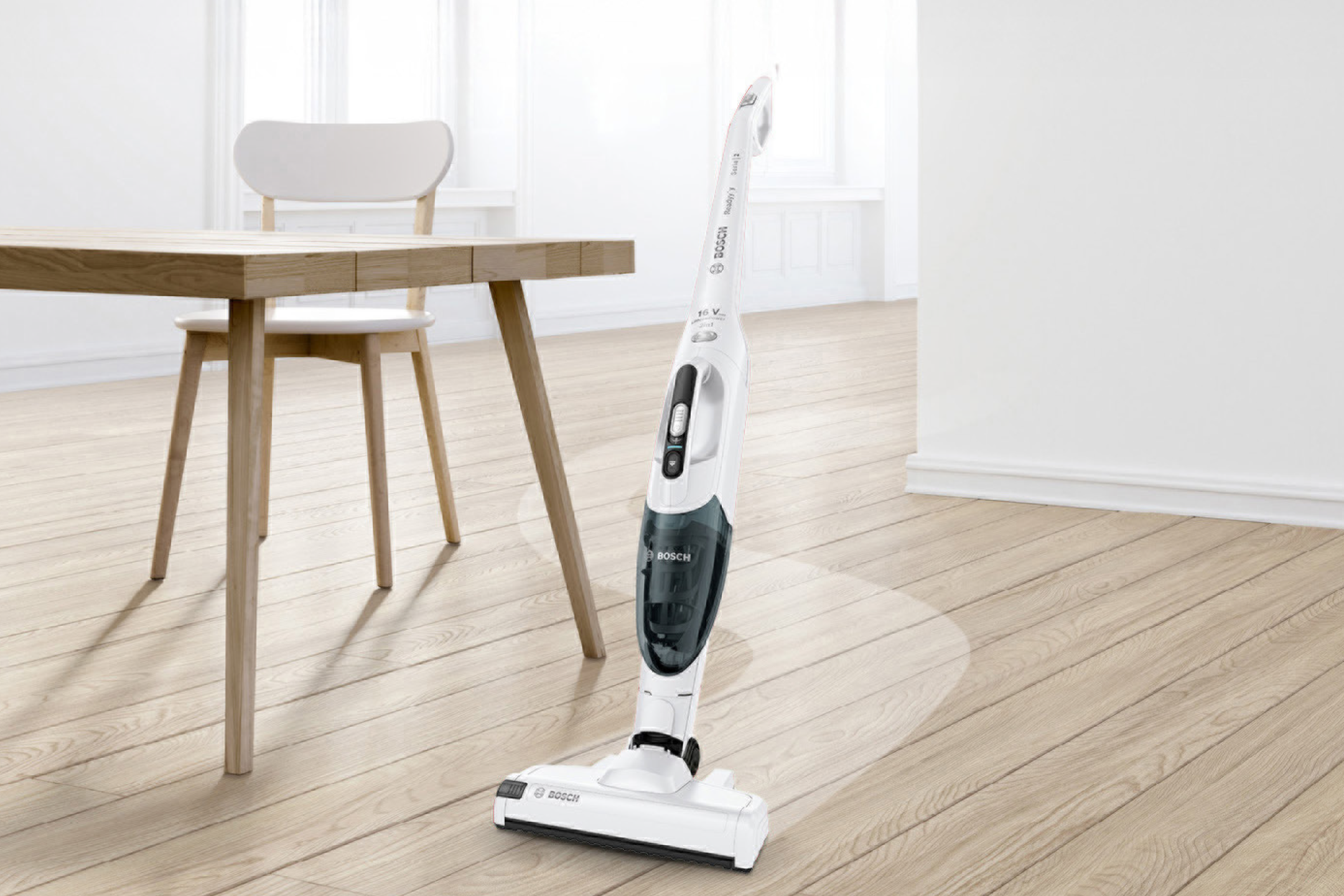 Ασύρματη ηλεκτρική σκούπα σε ένα φωτεινό δωμάτιο με ξύλινο τραπέζι και καρέκλα.