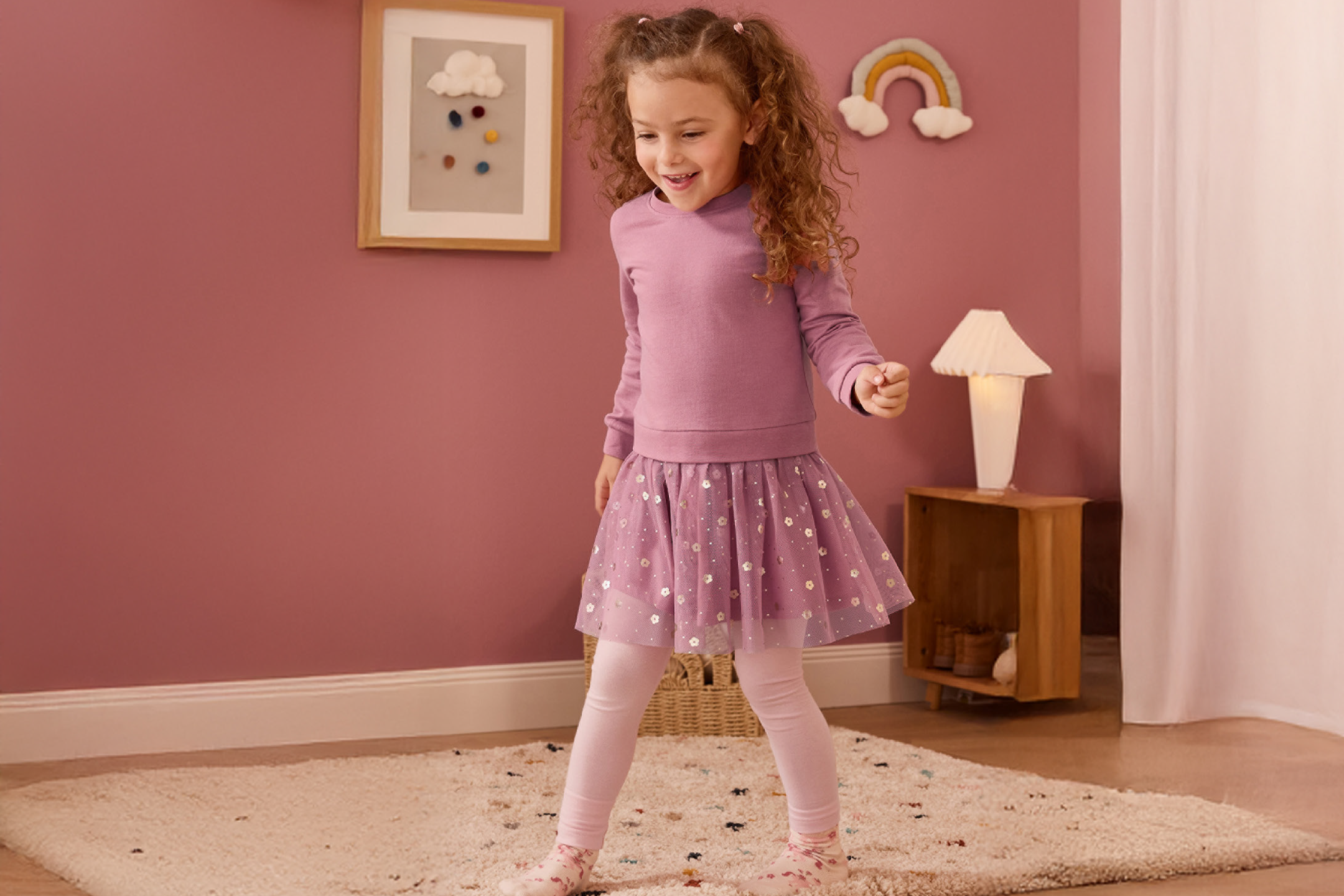 Χαρούμενο κορίτσι με μοβ μπλούζα, φούστα με πούλιες και κολάν σε παιδικό δωμάτιο.