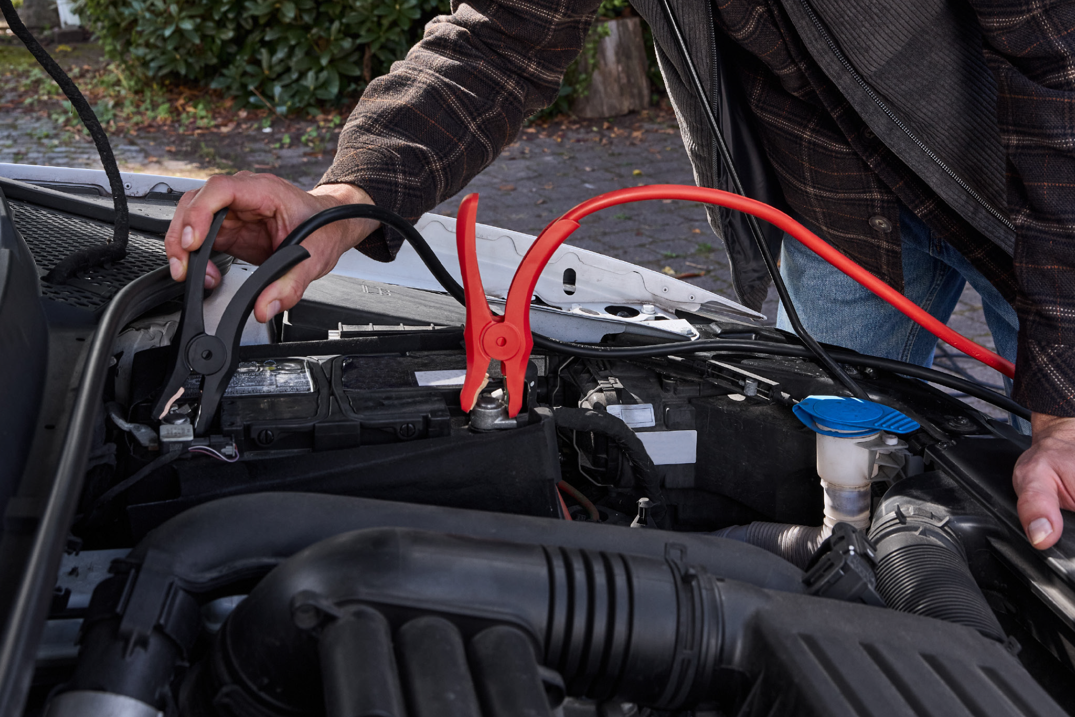 Άντρας συνδέει καλώδια εκκίνησης σε μπαταρία αυτοκινήτου.