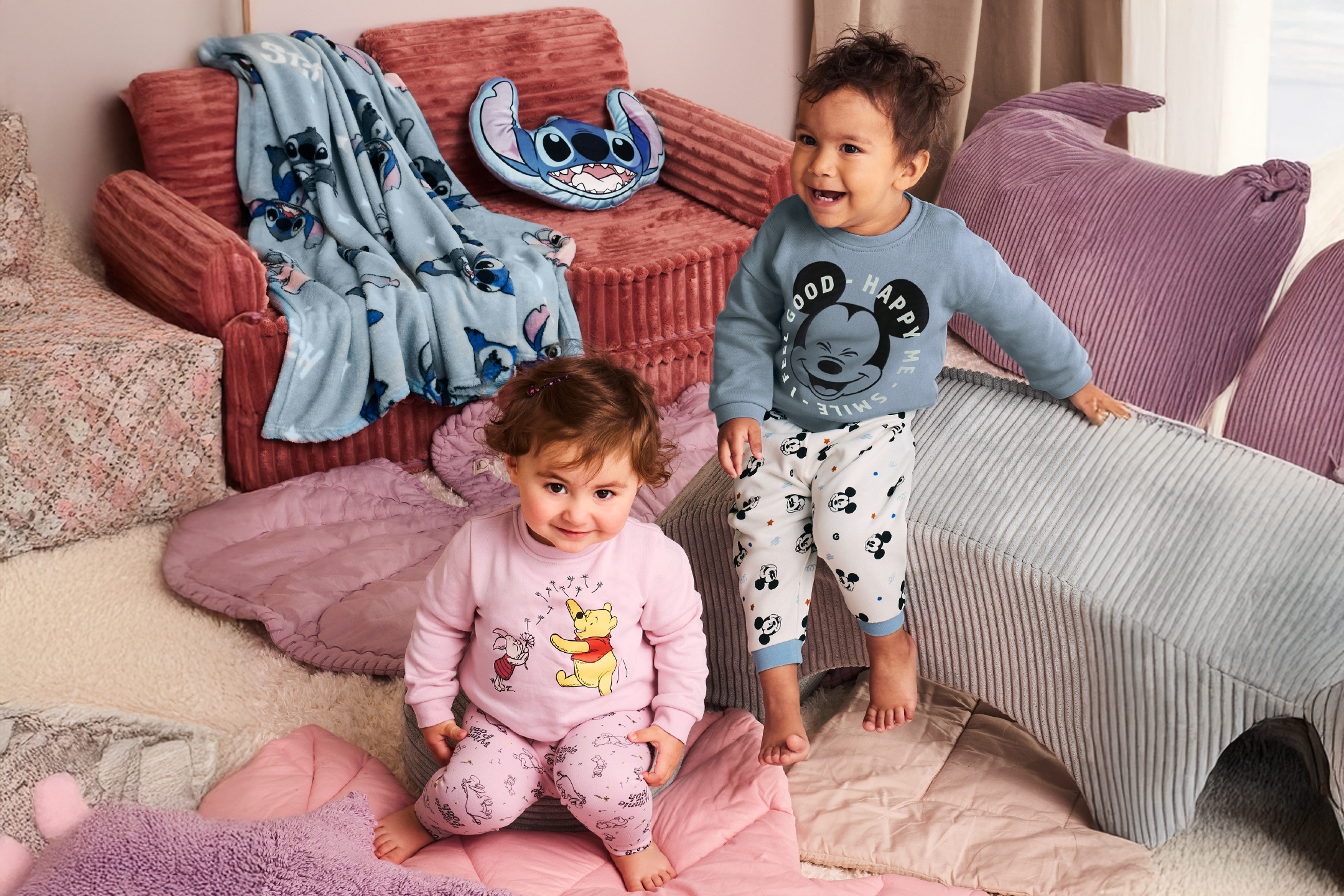 Δύο παιδιά με πιτζάμες με σχέδια κινουμένων σχεδίων, που κάθονται ανάμεσα σε μαξιλάρια και κουβέρτες.