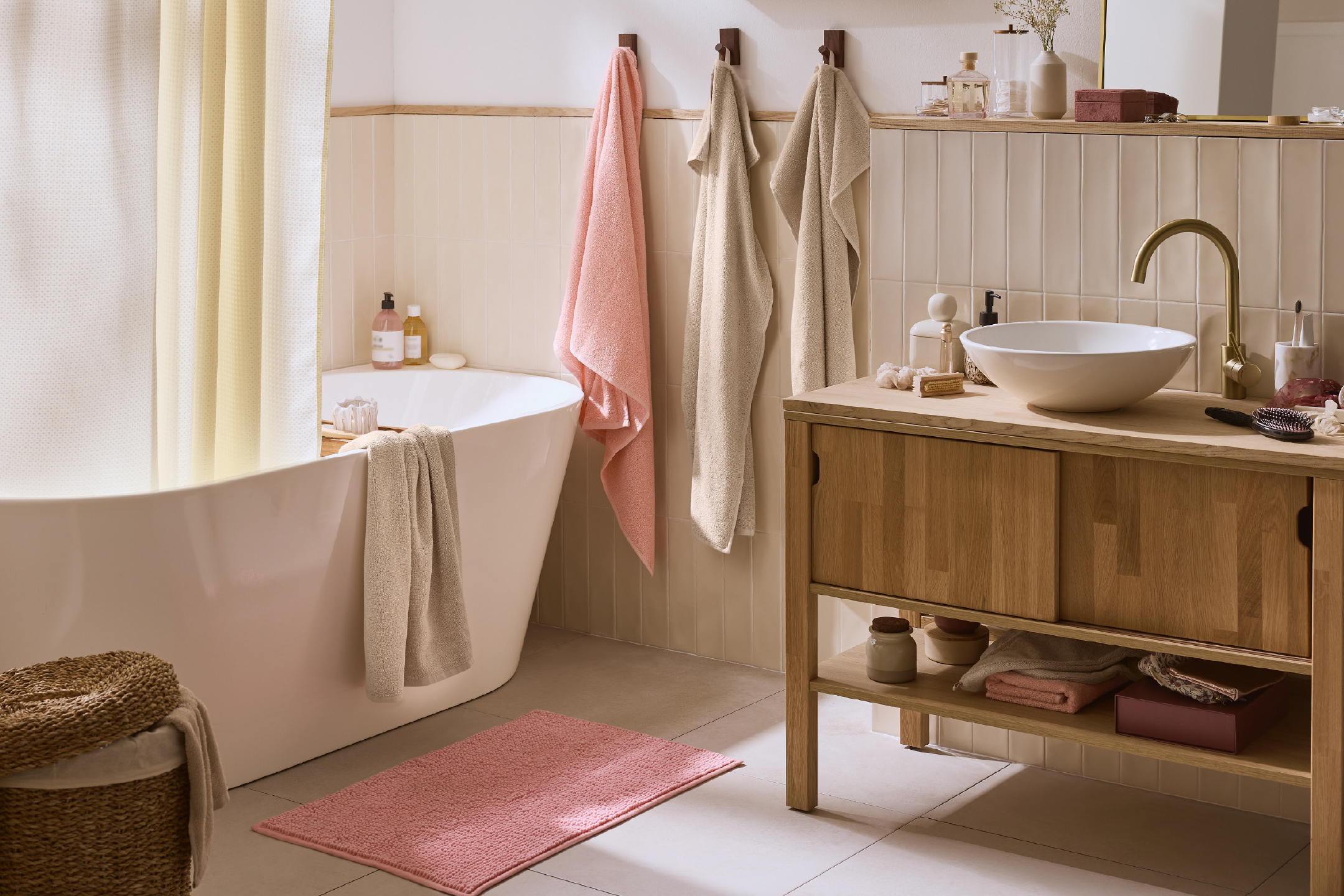 Μπάνιο με λευκή μπανιέρα, ξύλινο νιπτήρα, ροζ χαλάκι και πετσέτες.