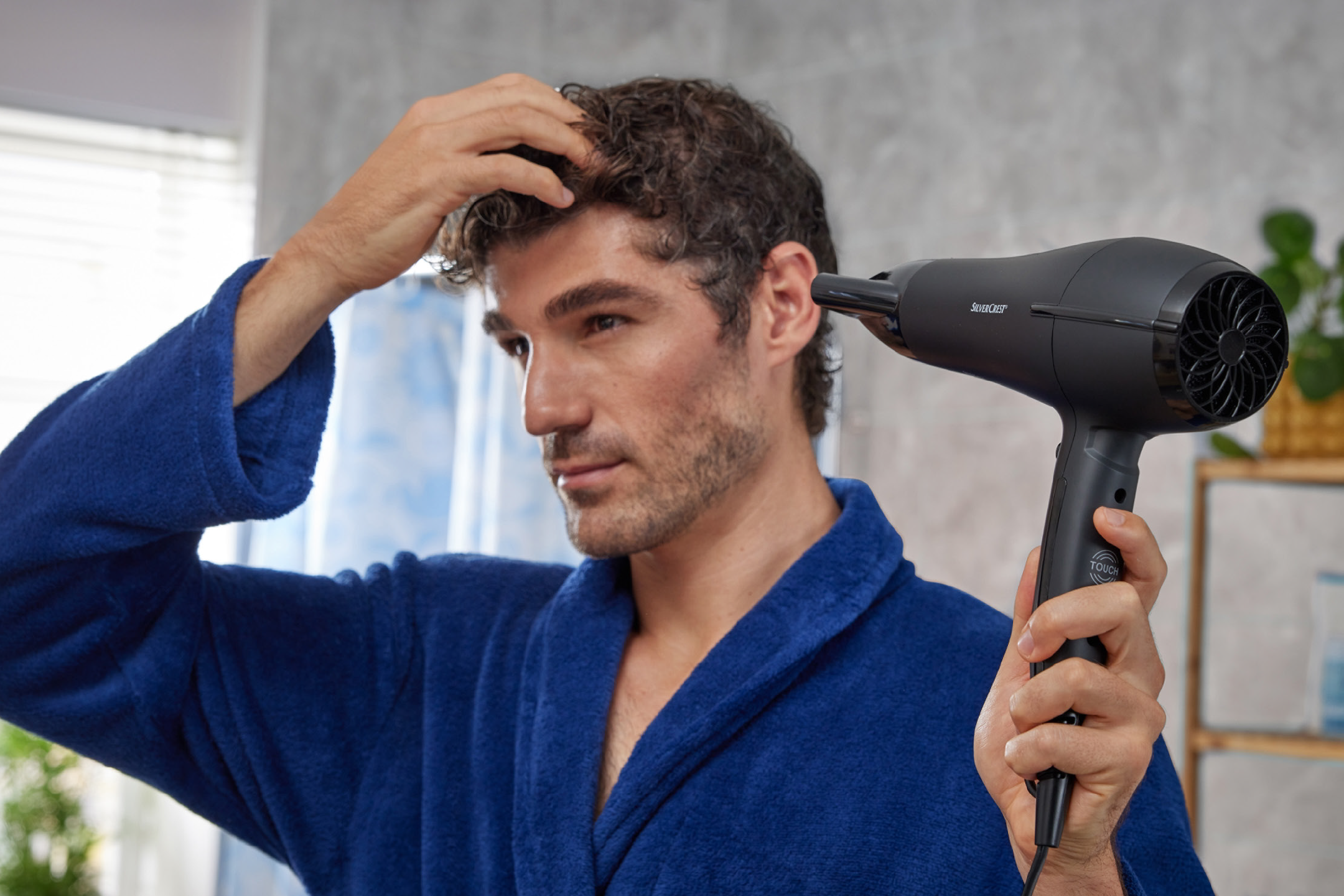 Άντρας με μπλε μπουρνούζι στεγνώνει τα μαλλιά του με πιστολάκι.