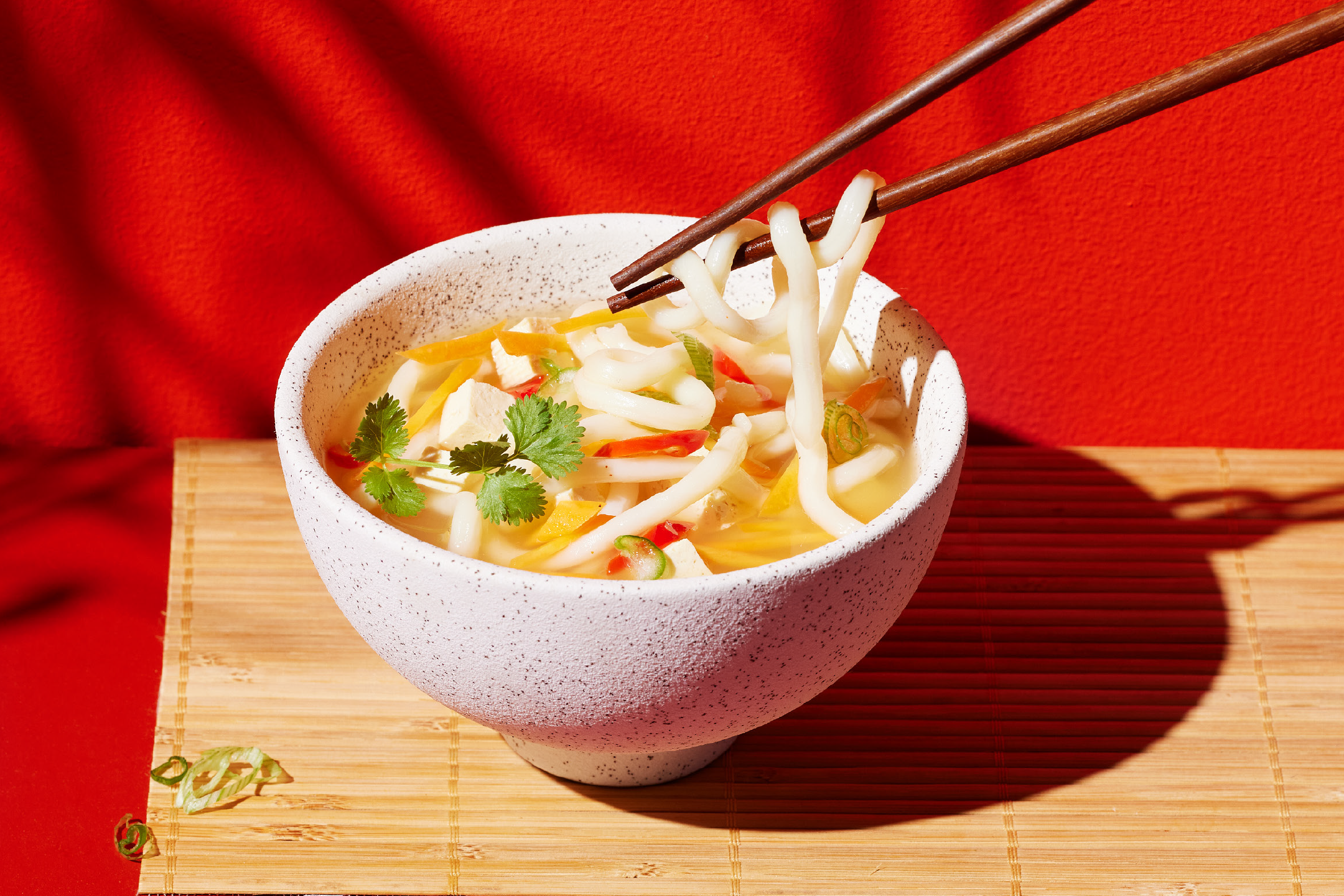 Μπολ με νουντλς udon, τόφου, λαχανικά και κόλιανδρο, με ξυλάκια να σηκώνουν νουντλς.