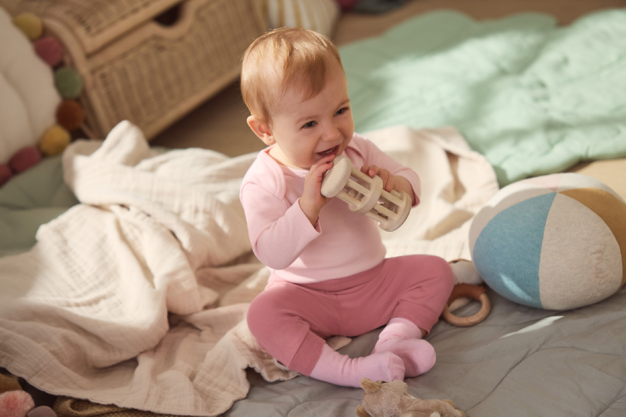 Χαρούμενο μωρό με ροζ ρούχα παίζει με ξύλινη κουδουνίστρα σε παιδικό δωμάτιο.