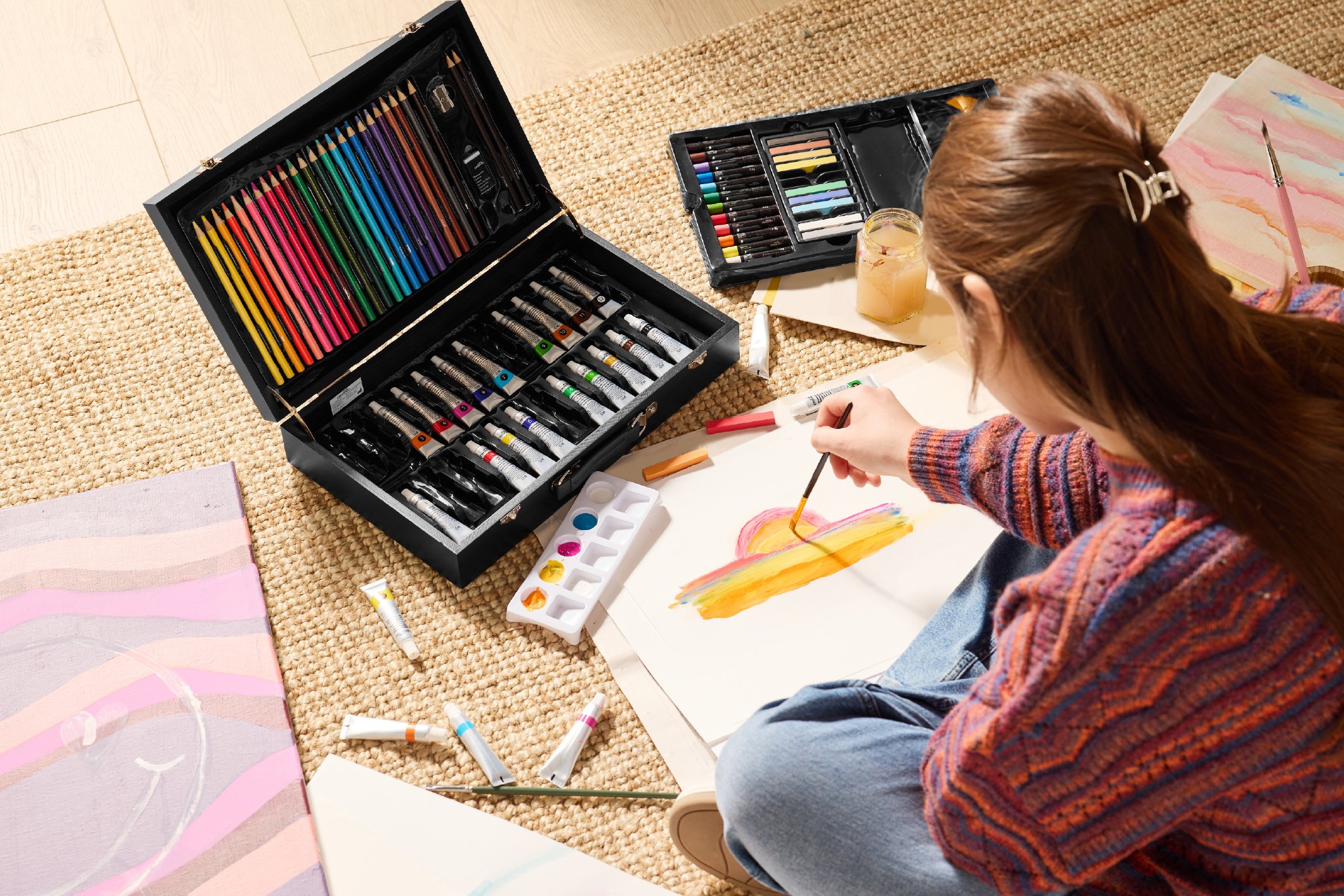 Σετ ζωγραφικής με χρωματιστά μολύβια, μπογιές και παστέλ, που χρησιμοποιείται από άτομο που ζωγραφίζει στο πάτωμα.