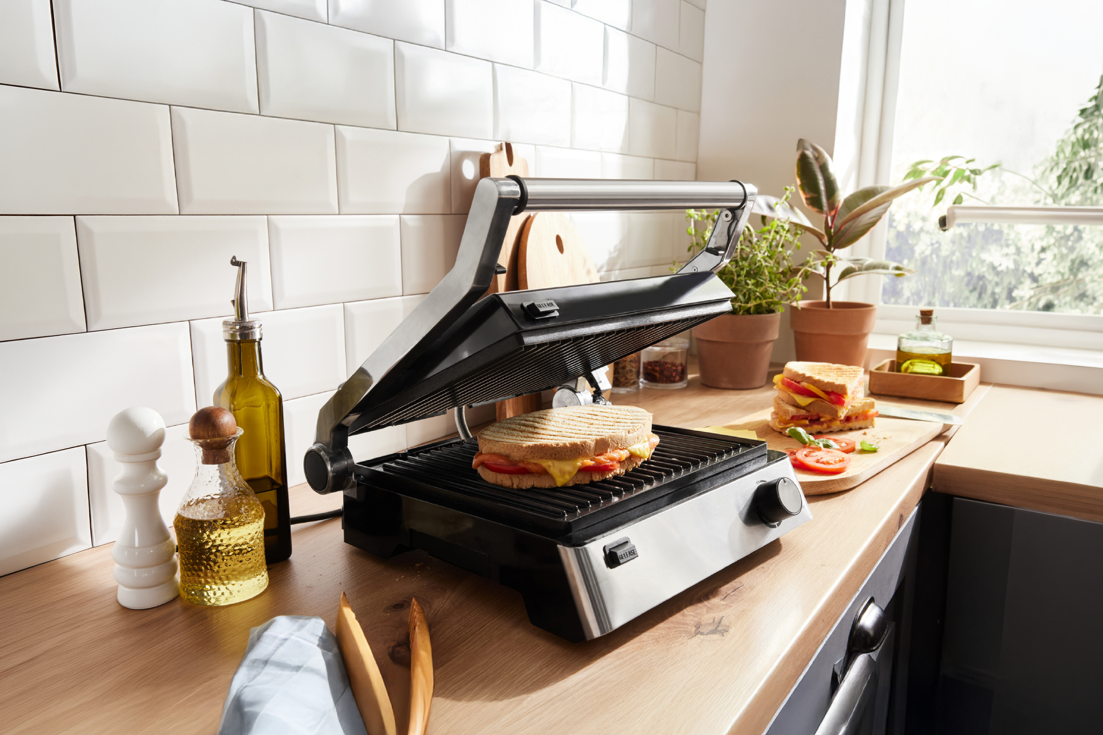 Τοστιέρα με σάντουιτς, μπουκάλια λαδιού και φυτά σε πάγκο κουζίνας.