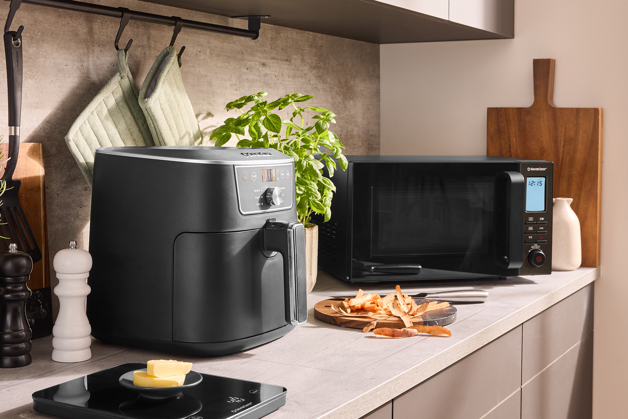 Μαύρη φριτέζα αέρος και φούρνος μικροκυμάτων σε μοντέρνο πάγκο κουζίνας με βασιλικό και σκεύη.