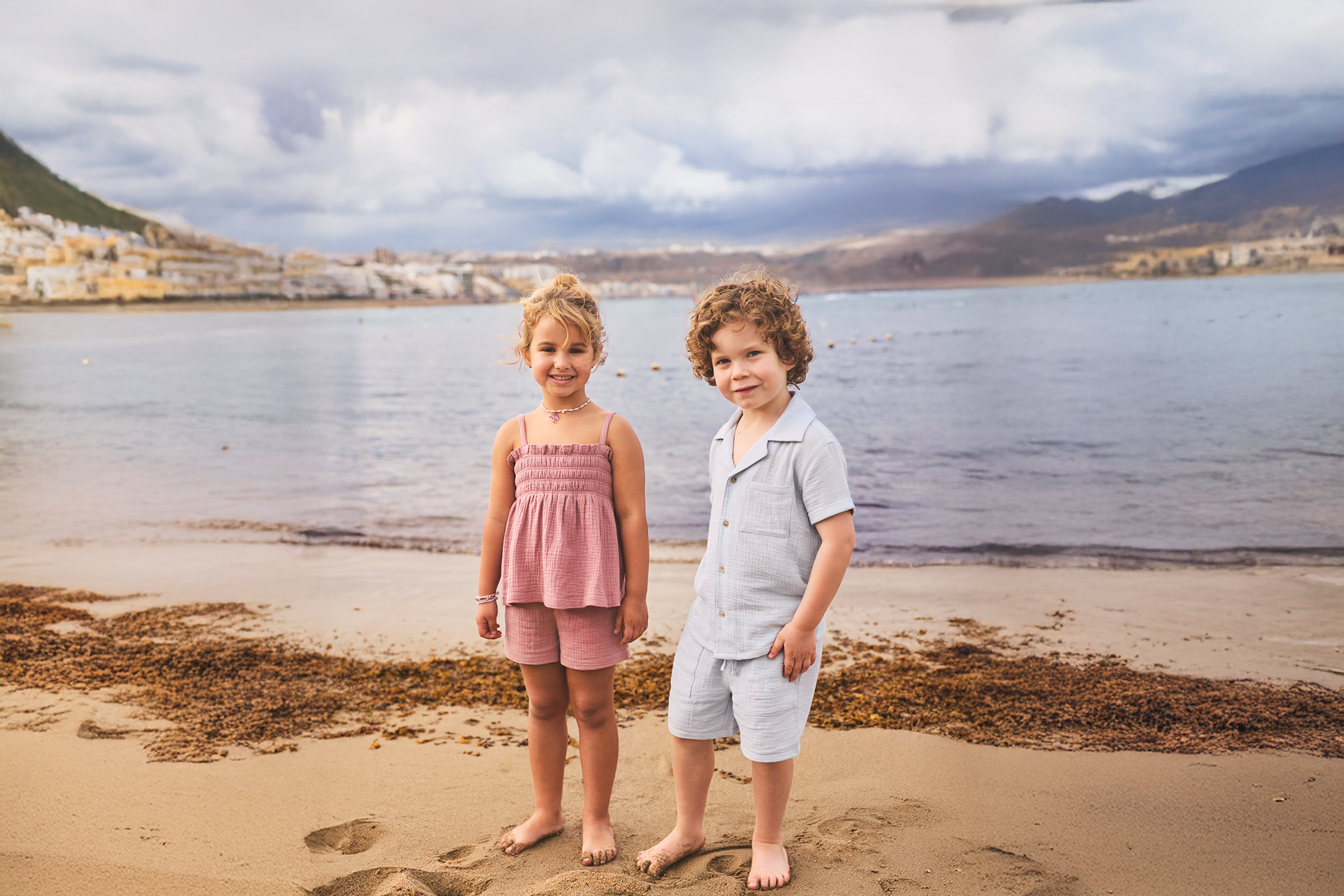 Παιδικά ρούχα παραλίας: κορίτσι με ροζ τοπ και σορτς, αγόρι με γαλάζιο σετ πουκάμισο-σορτς.