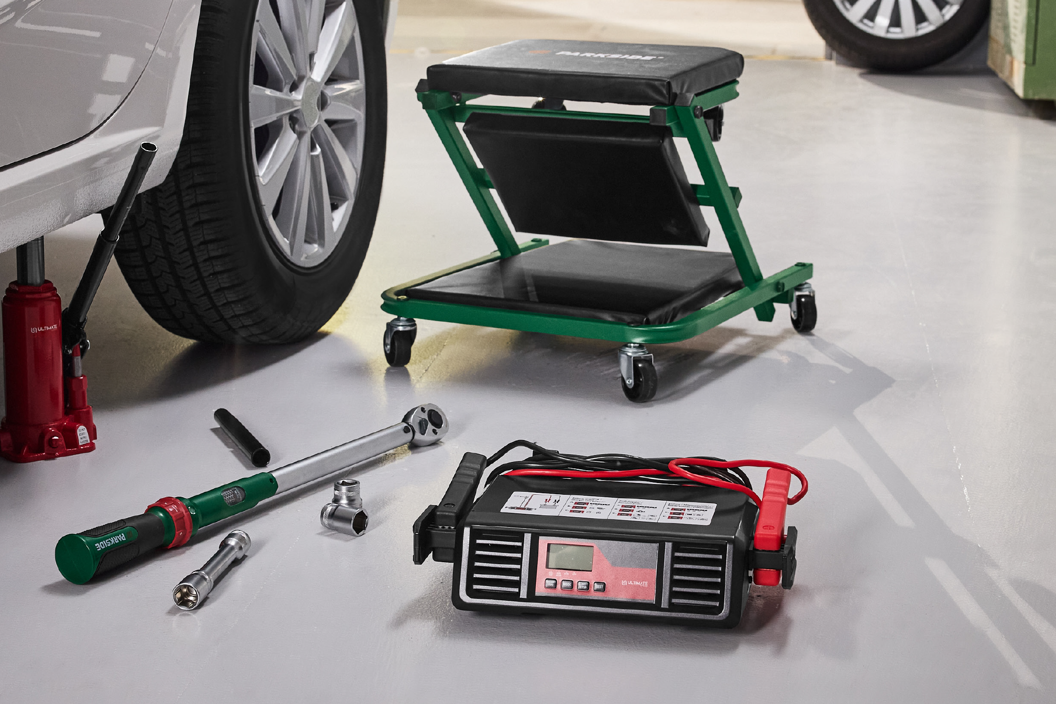 Εργαλεία αυτοκινήτου: γρύλος, κλειδί ροπής, φορτιστής μπαταρίας και τροχήλατο κάθισμα συνεργείου.