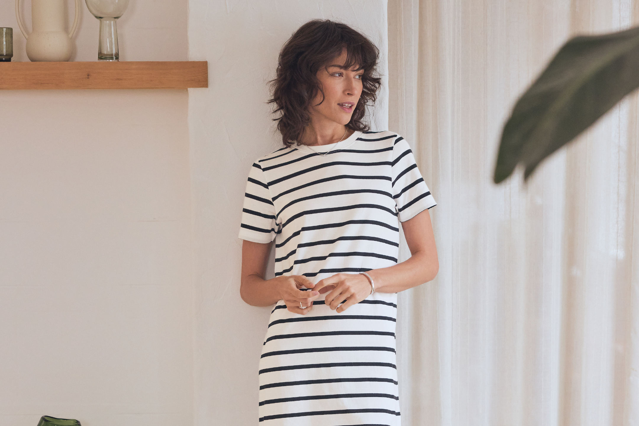 Γυναίκα με ριγέ φόρεμα, στέκεται δίπλα σε ράφι με διακοσμητικά.