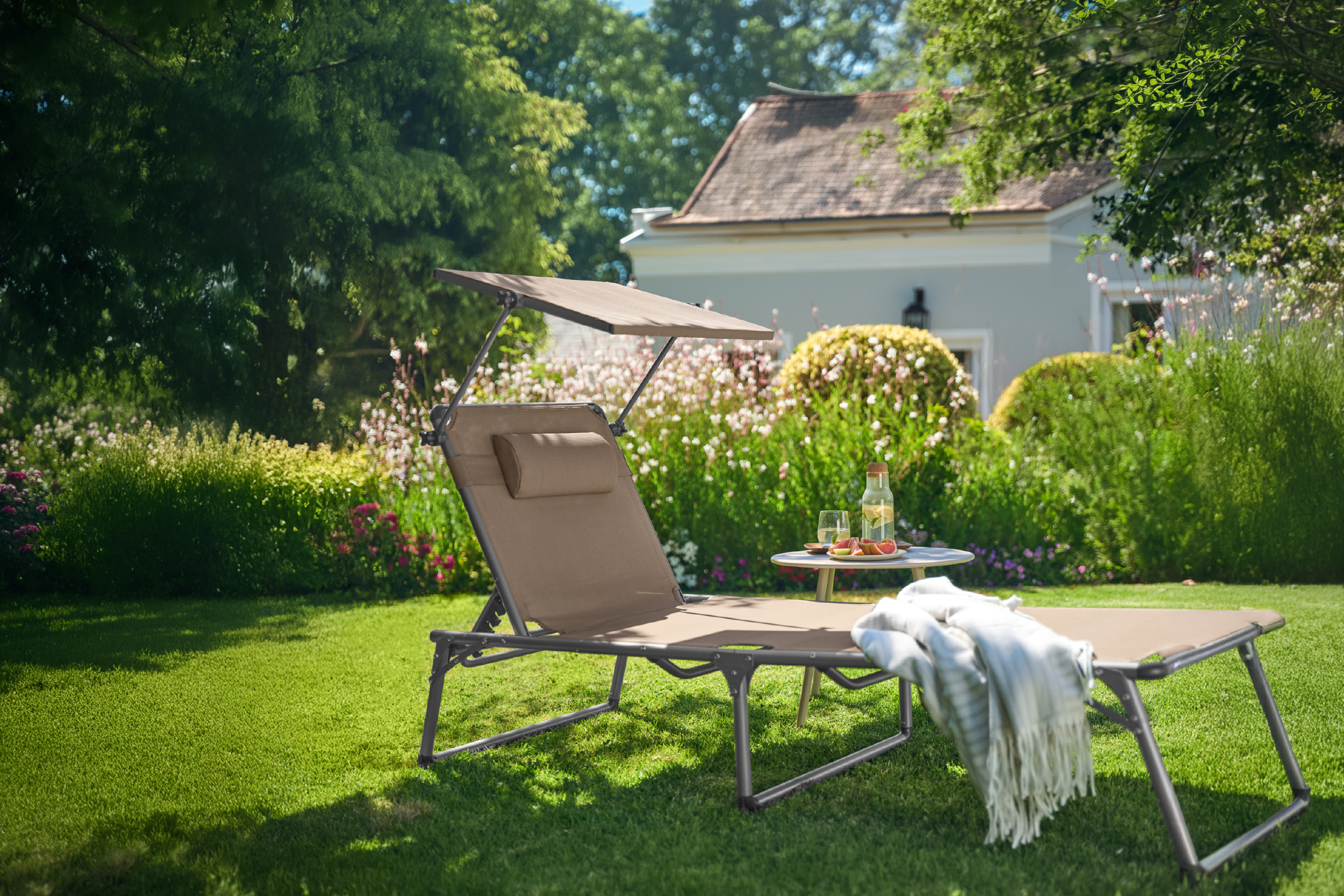 Ξαπλώστρα κήπου με σκίαστρο και τραπεζάκι με ποτά σε καταπράσινο κήπο.