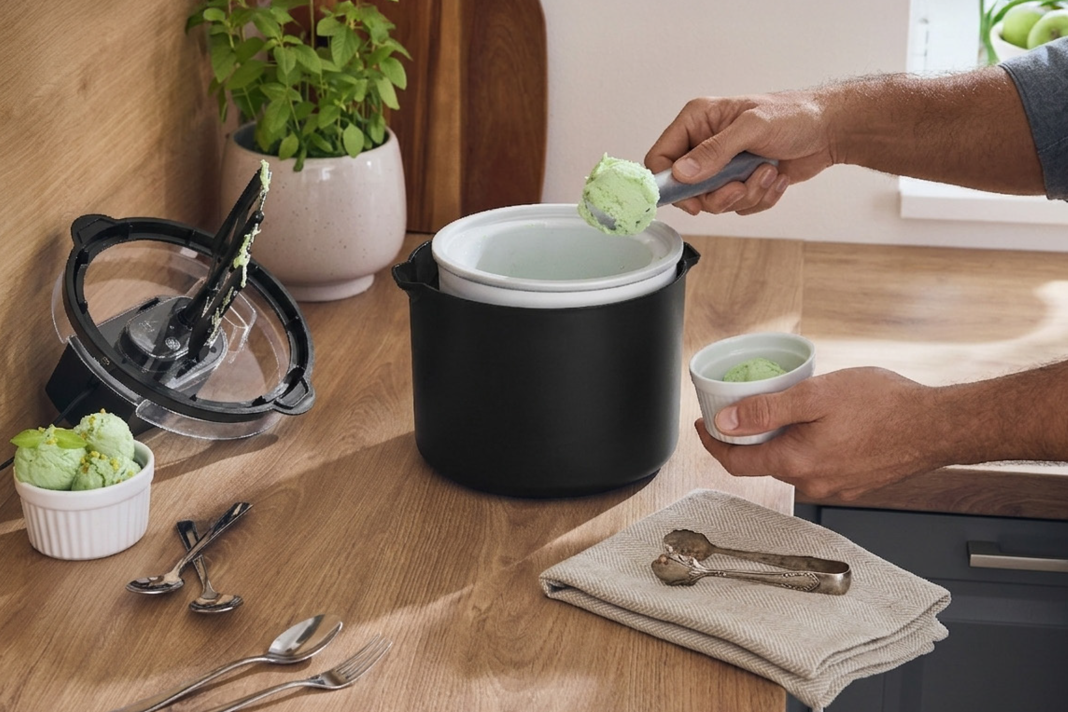 Άνδρας σερβίρει παγωτό φιστίκι από παγωτομηχανή σε μπολ, με κουτάλια και σκεύη στην κουζίνα.