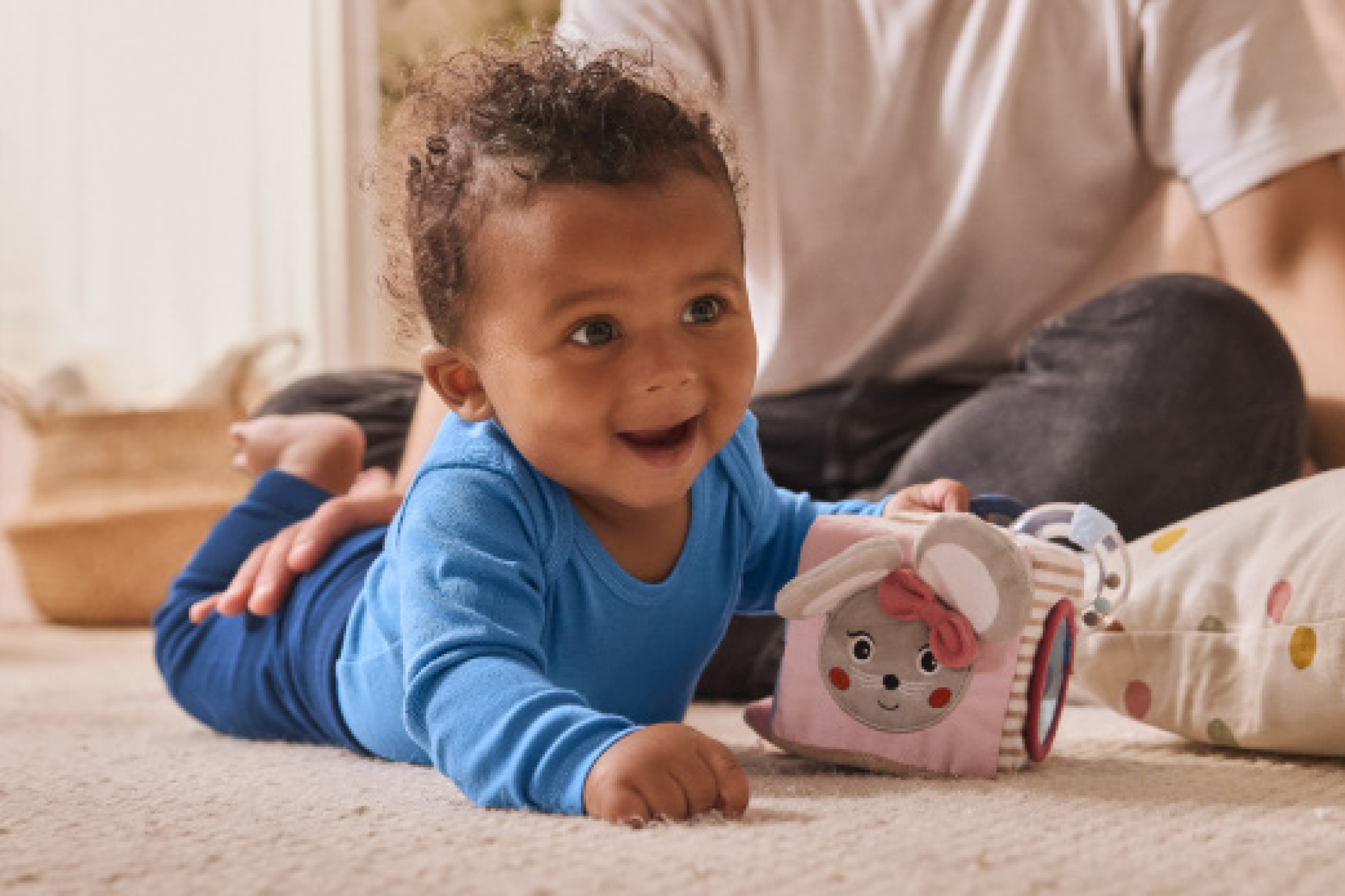 Χαμογελαστό μωρό σε μπλε φορμάκι παίζει με ένα μαλακό παιχνίδι σε σχήμα κύβου.