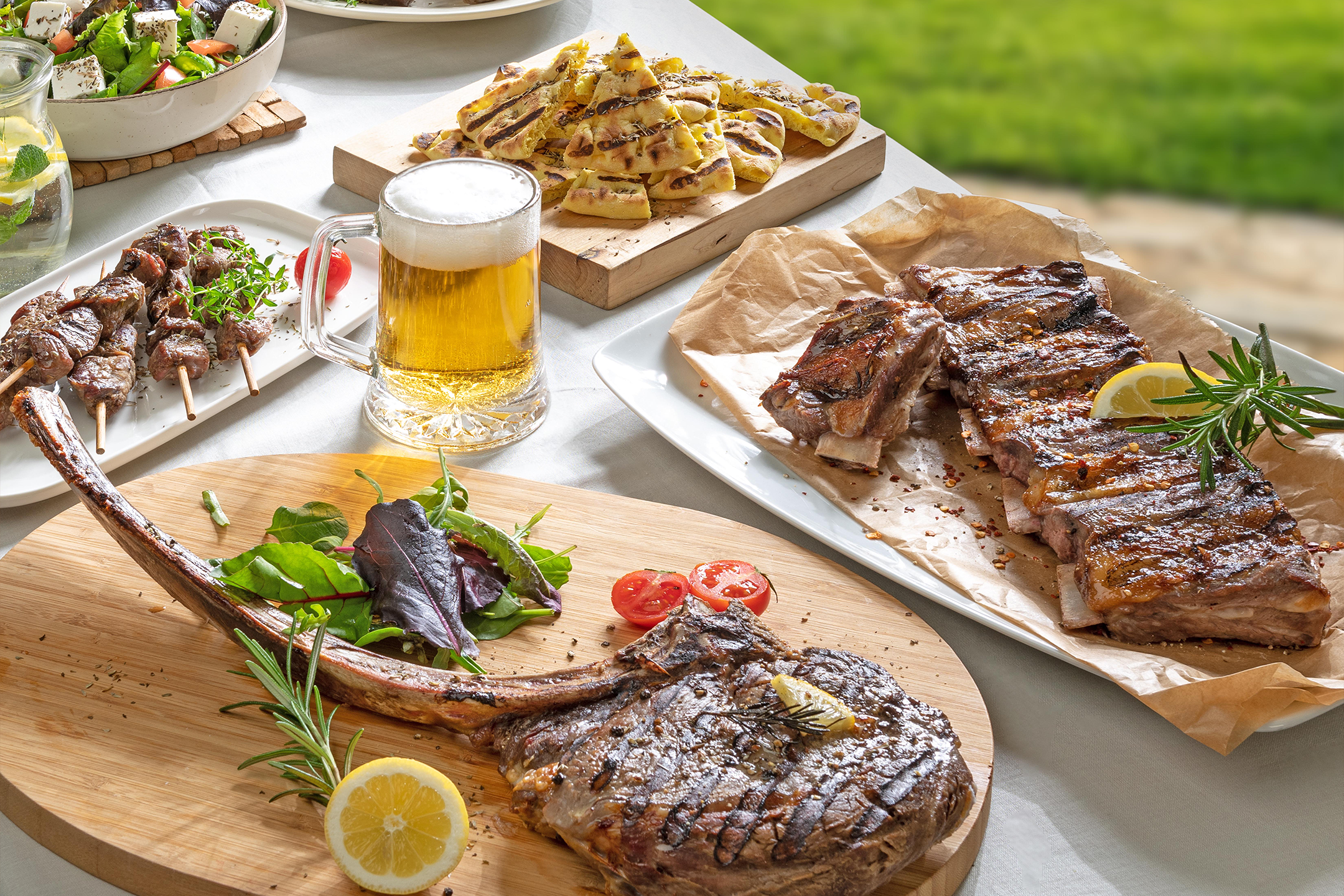 Ψητά κρέατα, μπύρα, σαλάτα και ψωμί σε εξωτερικό τραπέζι.