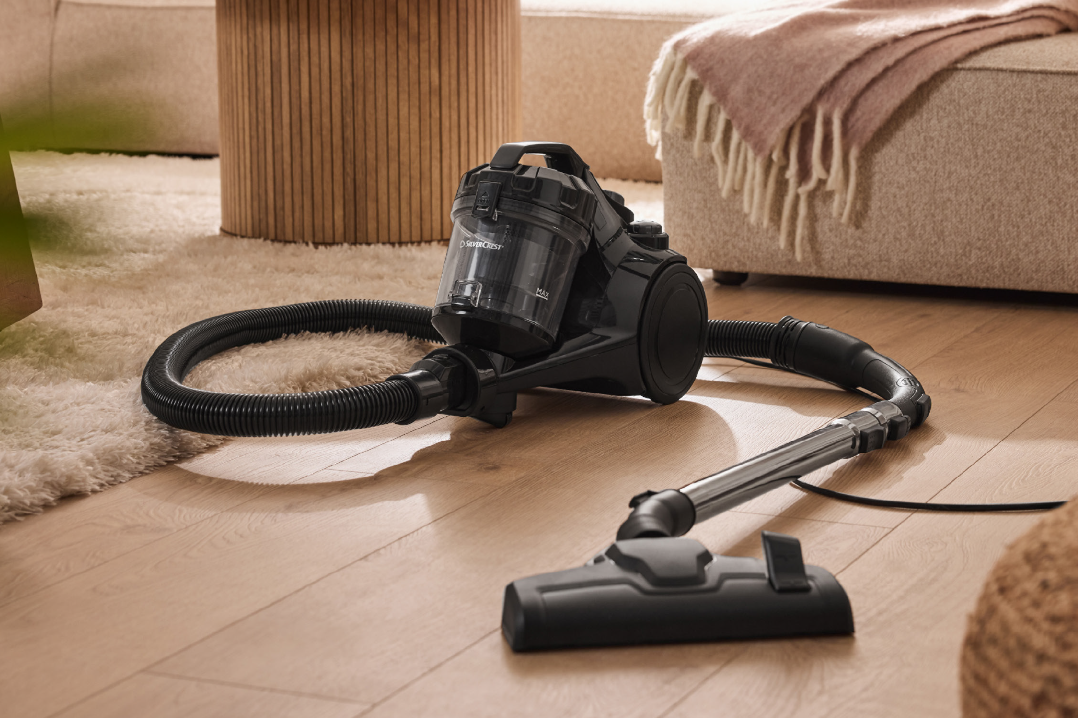 Μαύρη ηλεκτρική σκούπα δαπέδου με κάδο σε ξύλινο πάτωμα και χαλί.