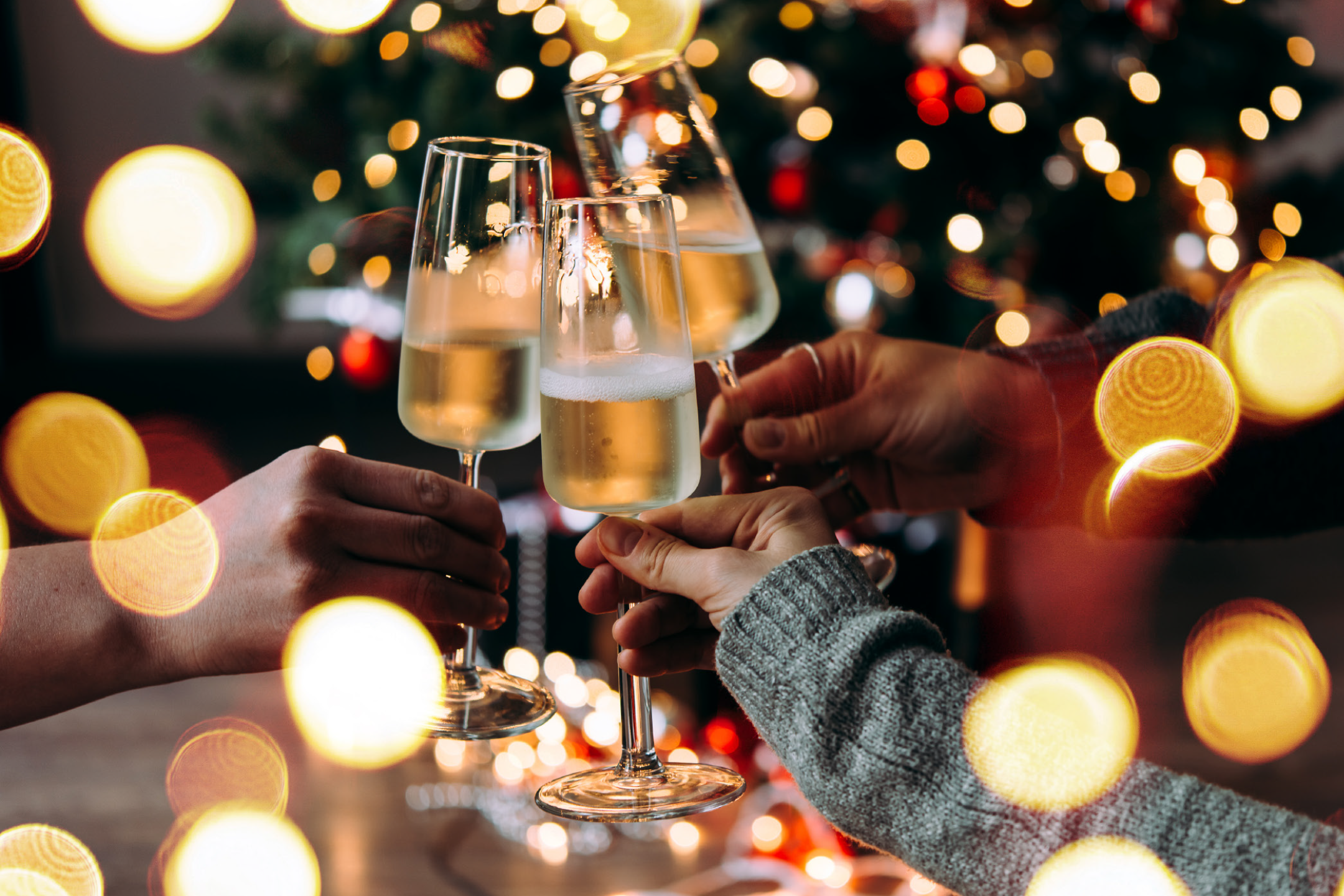 Ποτήρια σαμπάνιας που τσουγκρίζουν μπροστά σε ένα χριστουγεννιάτικο δέντρο με φώτα bokeh.