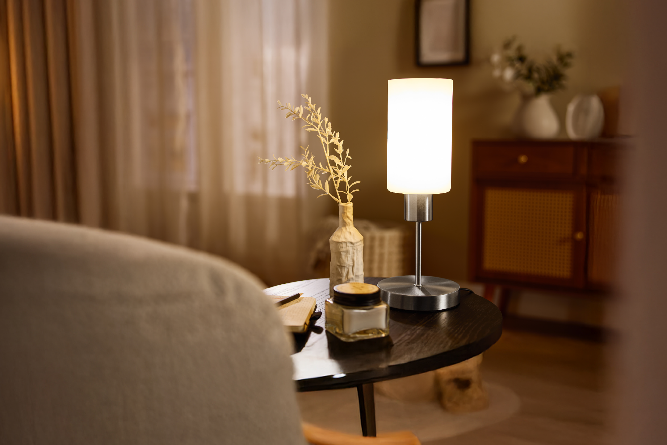 Φωτιστικό τραπεζιού με λευκό αμπαζούρ και διακοσμητικό βάζο σε σκούρο ξύλινο τραπέζι.