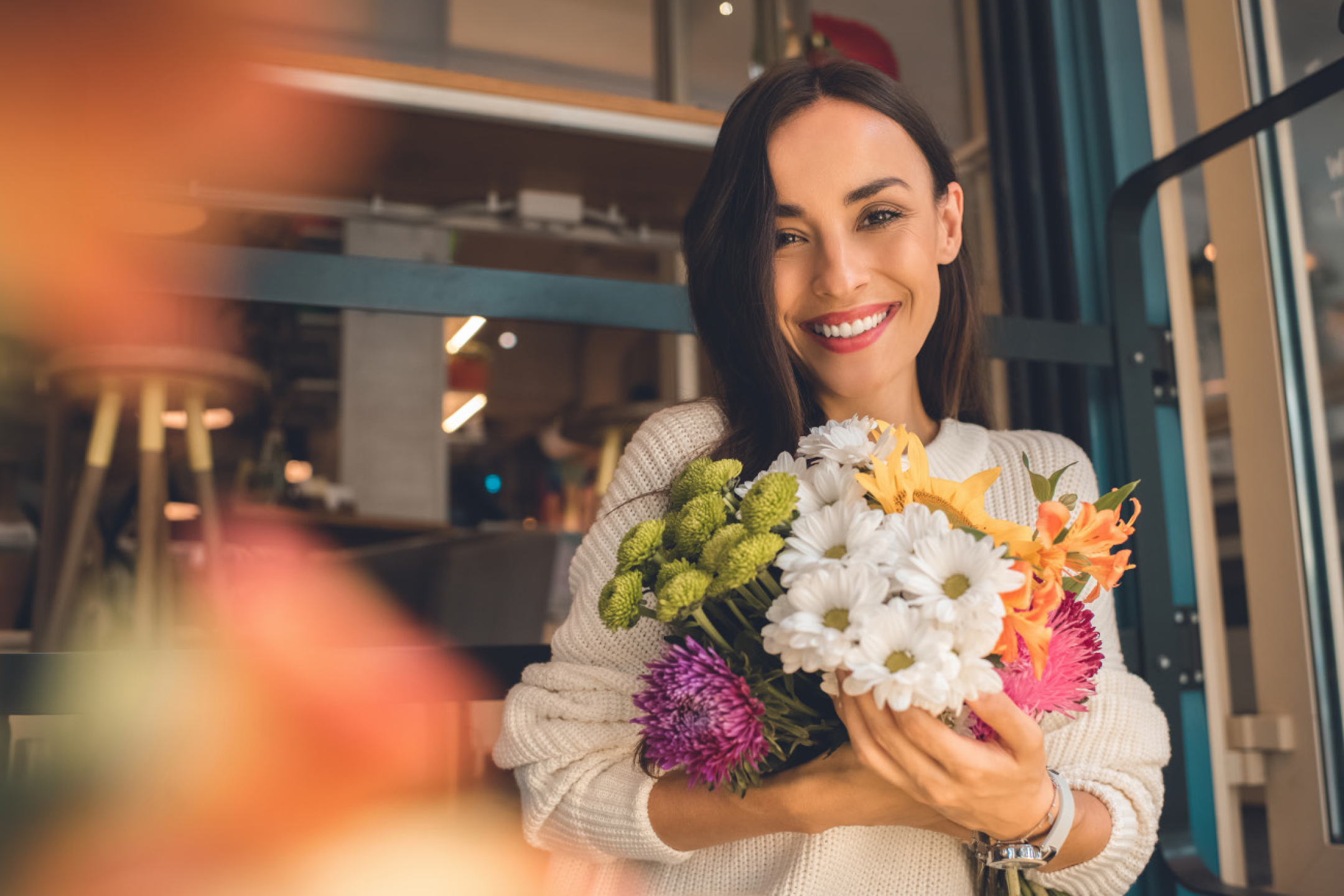 Χαμογελαστή γυναίκα κρατάει μια πολύχρωμη ανθοδέσμη.