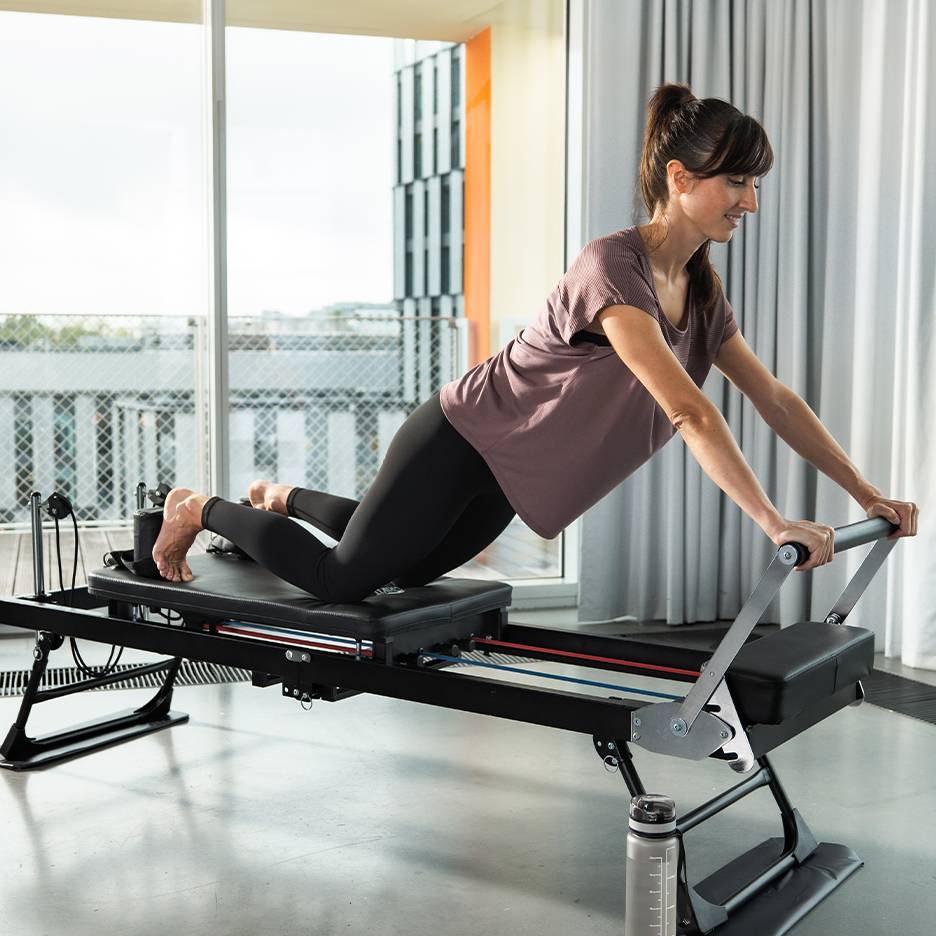 Γυναίκα κάνει Pilates σε reformer με ελατήρια και ιμάντες.