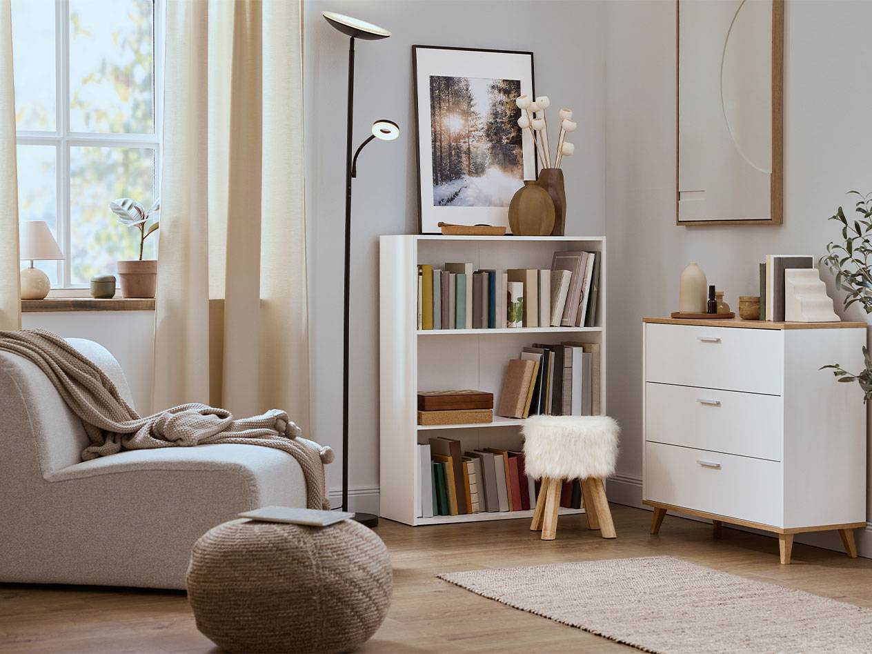 Άνετο σαλόνι με πολυθρόνα, ραφιέρα βιβλίων και συρταριέρα σε ουδέτερα χρώματα.